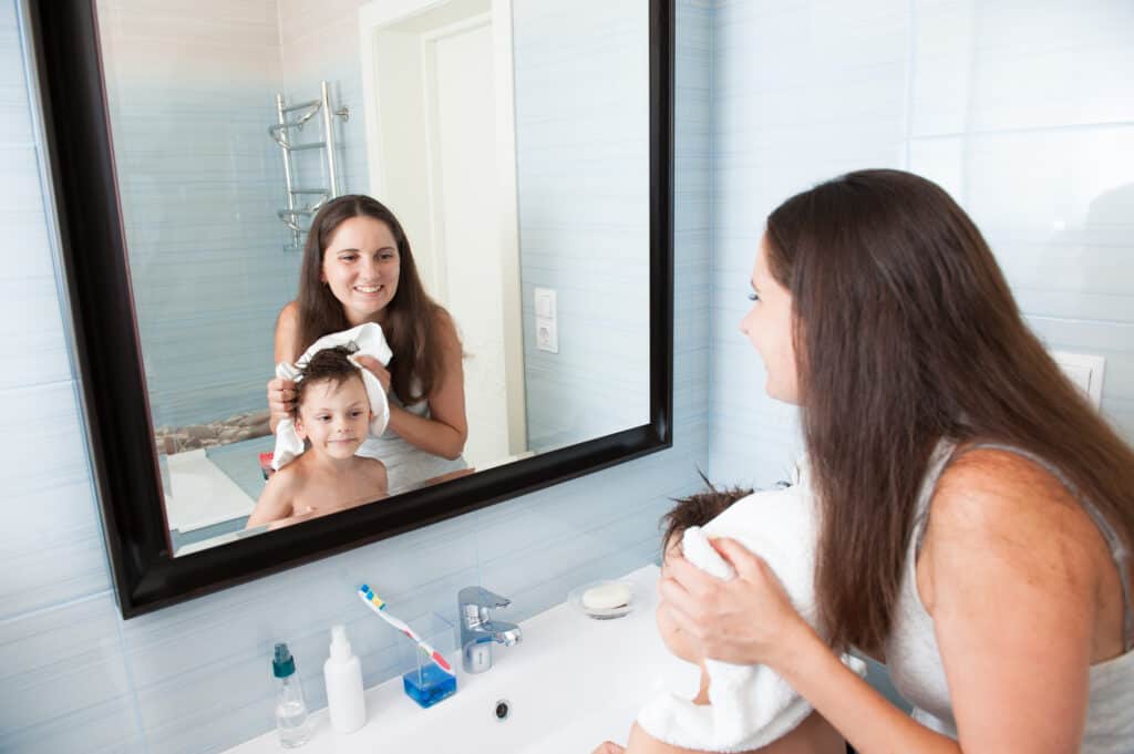 happy smiling mother drying her child's hair with white towel in bathroom
